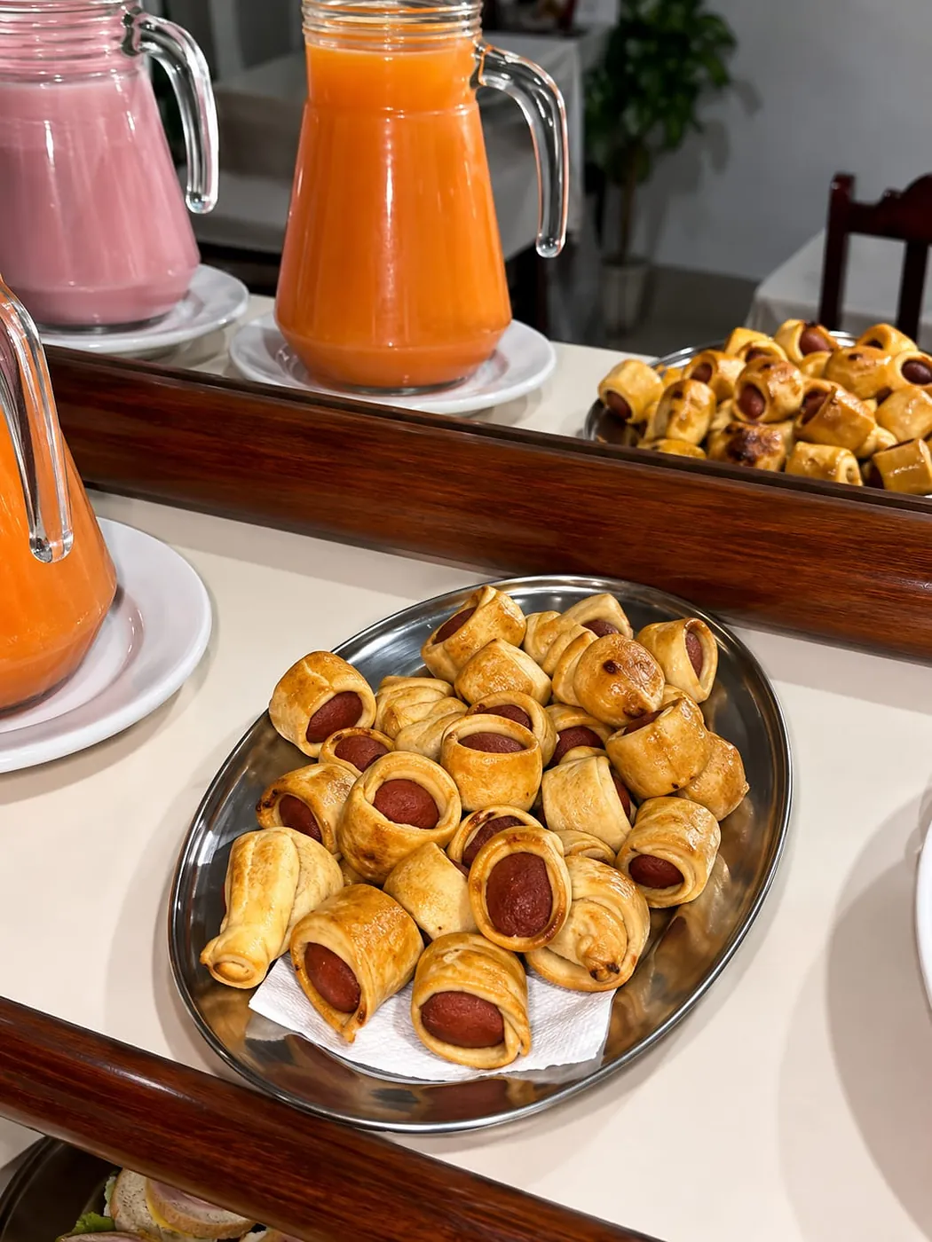 Enroladinhos de salsicha assados com jarras de suco ao fundo