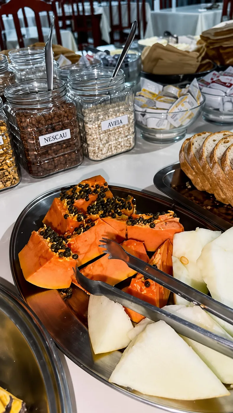 Mamão e melão cortados, com potes de granola, aveia e cereais no café do Hotel Tubarão