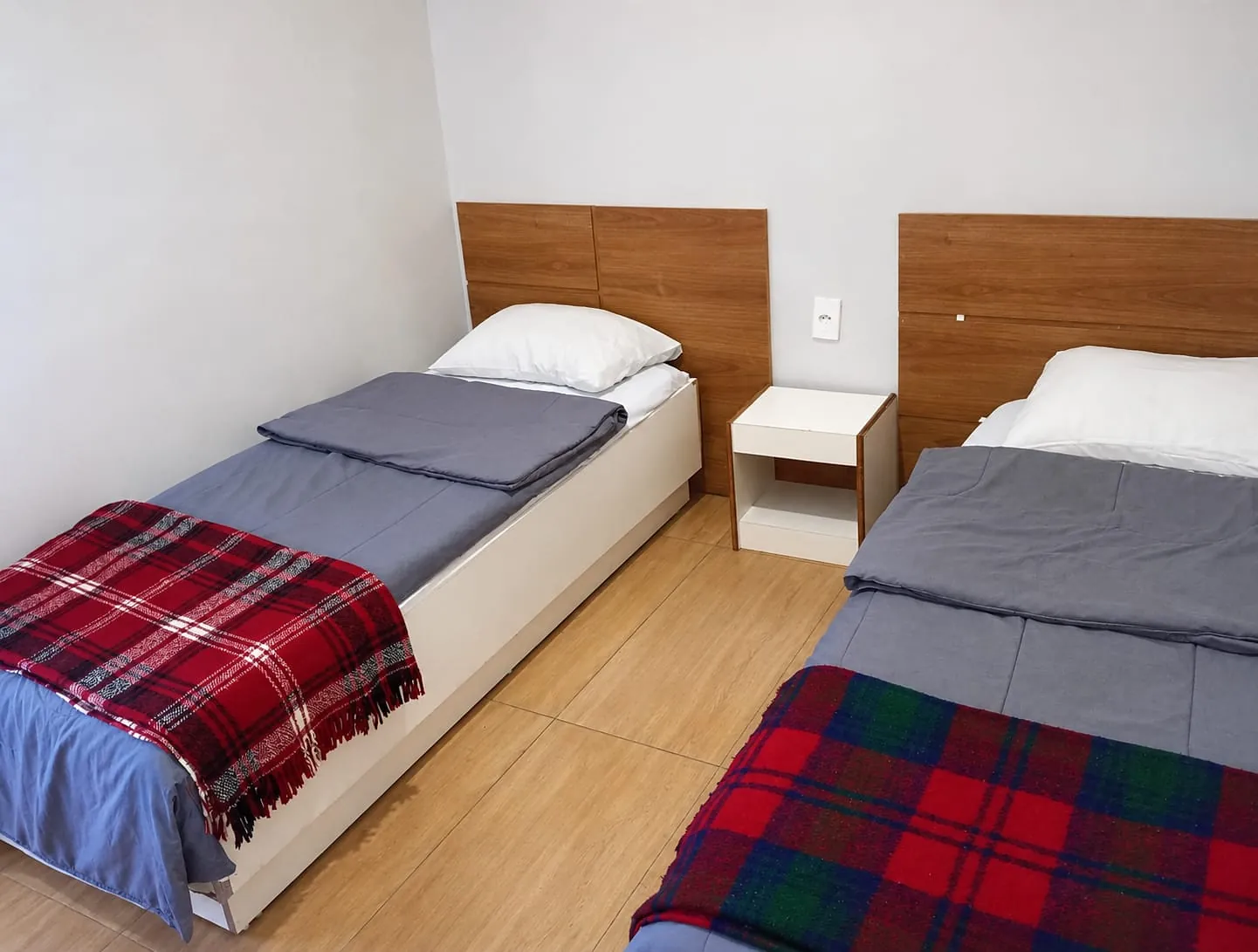 Quarto Econômico do Hotel Tubarão: duas camas de solteiro com cabeceira de madeira e criado-mudo
