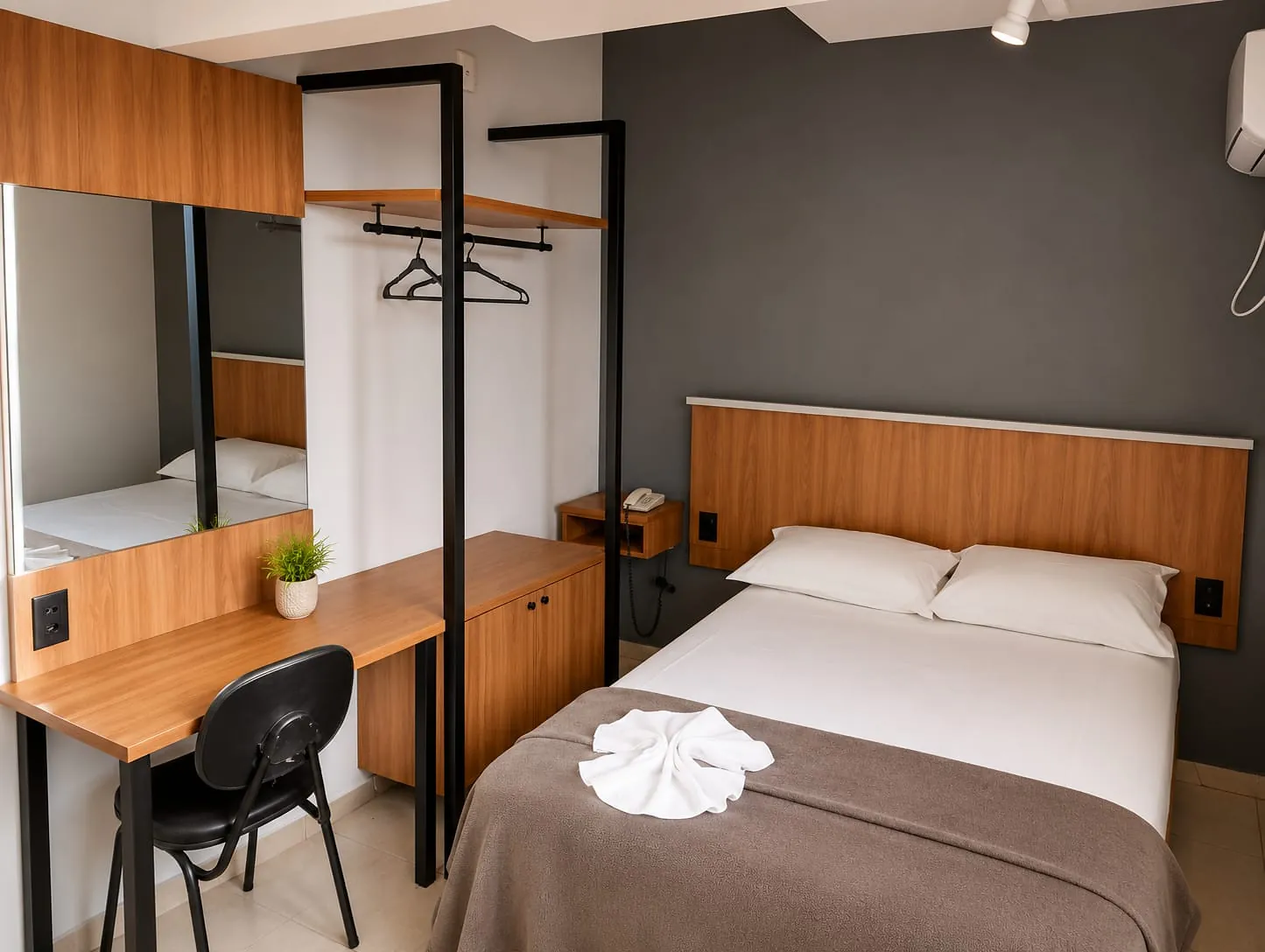Quarto Premium Casal do Hotel Tubarão: cama de casal com cabeceira de madeira, escrivaninha com espelho e arara para roupas
