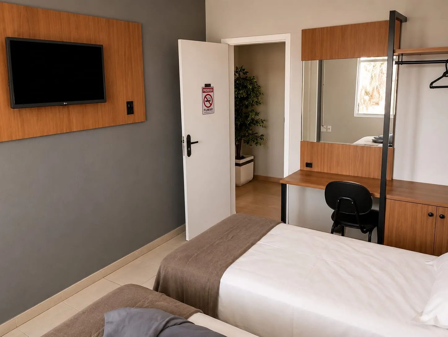 Entrada do Quarto Premium Família do Hotel Tubarão, com painel de TV em madeira e escrivaninha com cadeira